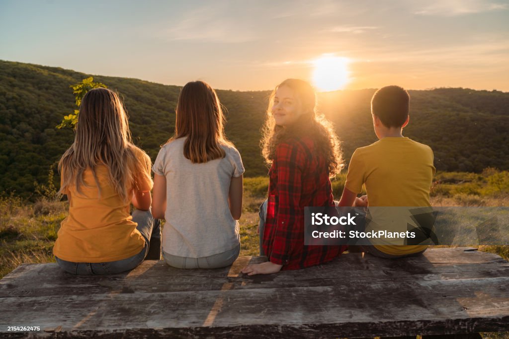 Rear view of a group of children during sunset in nature. One of them looking at camera