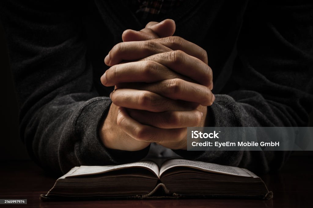 Cropped Image Pf Person With Hands Clasped On Book In Darkroom